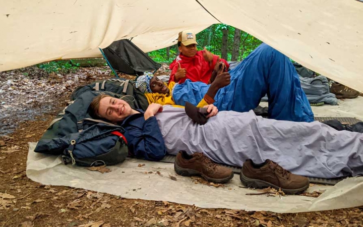 three teens rest under a tarp on an outward bound expedition 